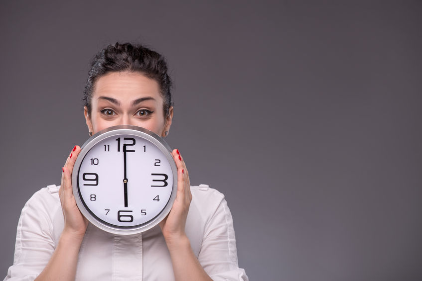 Portrait of business woman holding up clock and tracking employee time and attendance