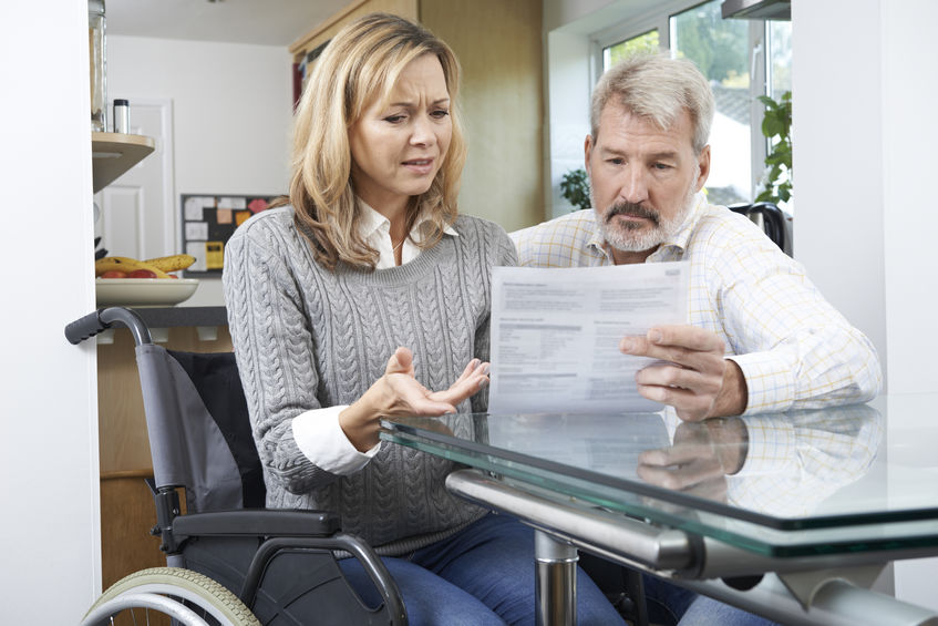 Frustrated Couple With Woman In Wheelchair Reading Insurance Bill