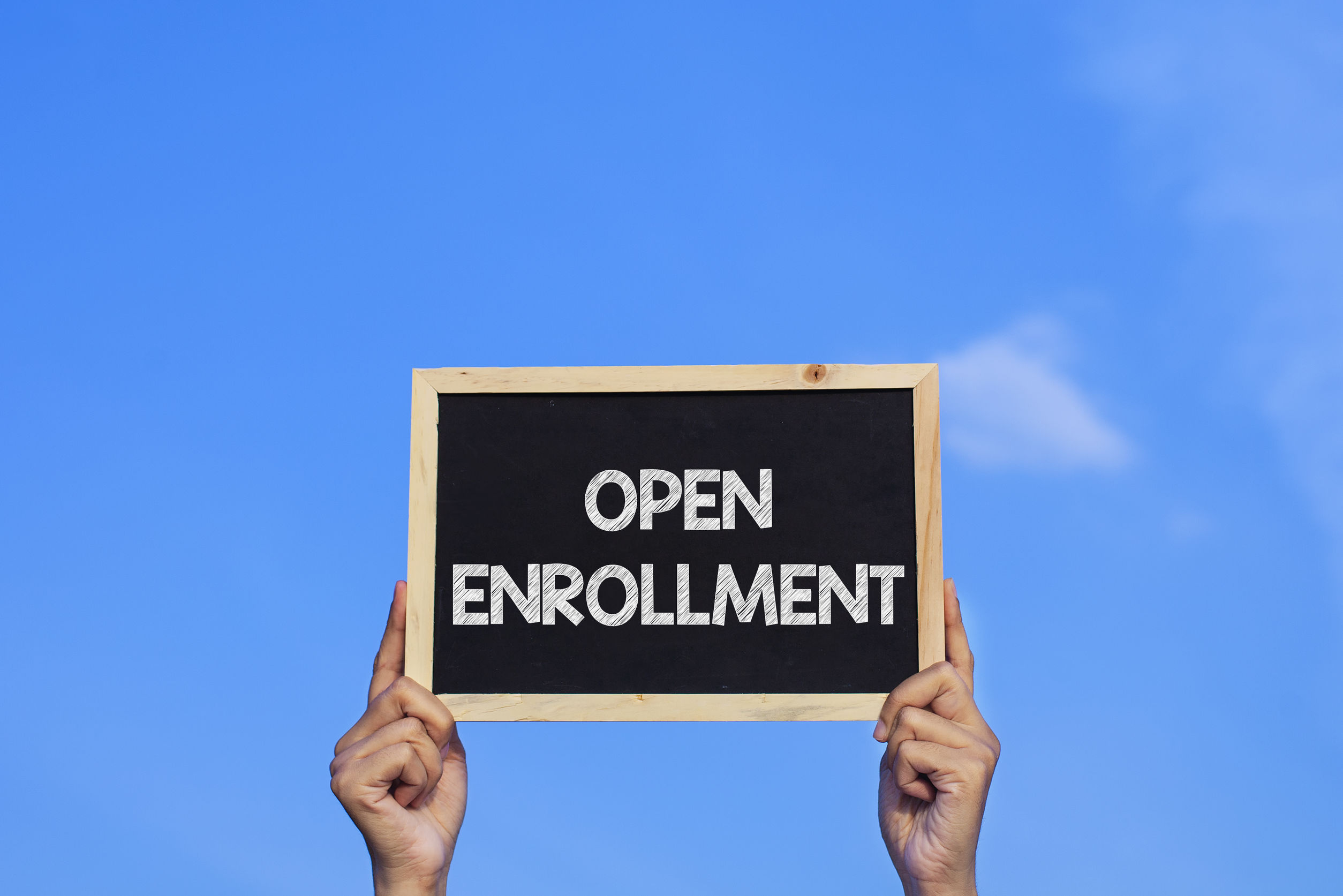 OPEN ENROLLMENT/ Man holding small blackboard on blue sky backgr