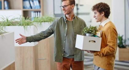 new employee enters a brightly lit office holding a box of belongings