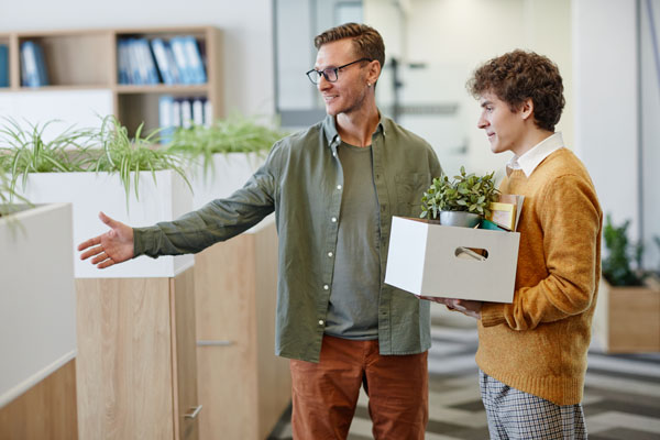 new employee enters a brightly lit office holding a box of belongings