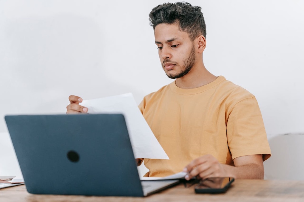 young male using laptop and looking at documents